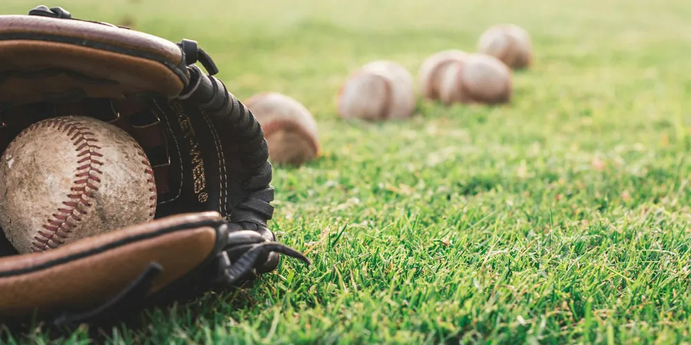 A leather baseball glove resting on green grass with a baseball tucked inside; several blurred balls in the background.