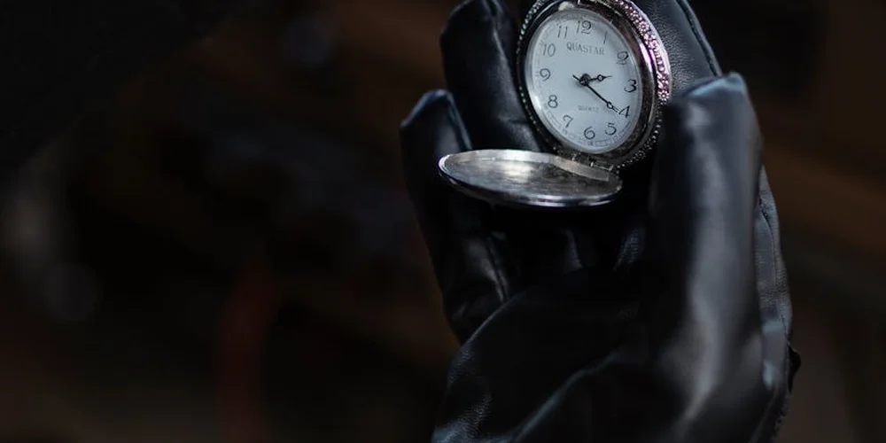 Close-up of a black leather glove holding an open pocket watch.
