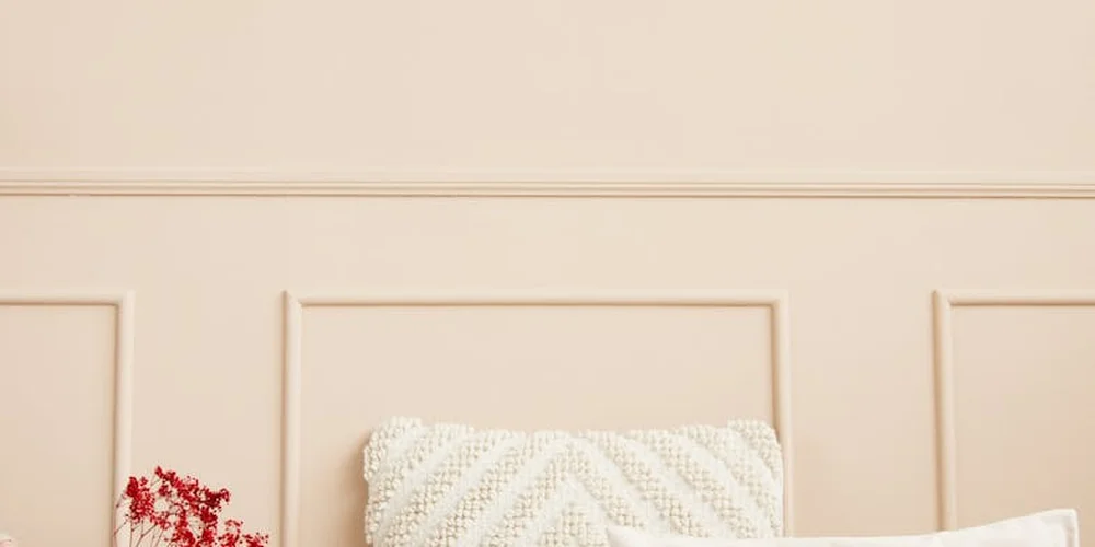 Close-up of a light beige sofa with a white knitted cushion against a matching wall, illustrating quick cleanup for spills on suede and faux suede cushion covers.