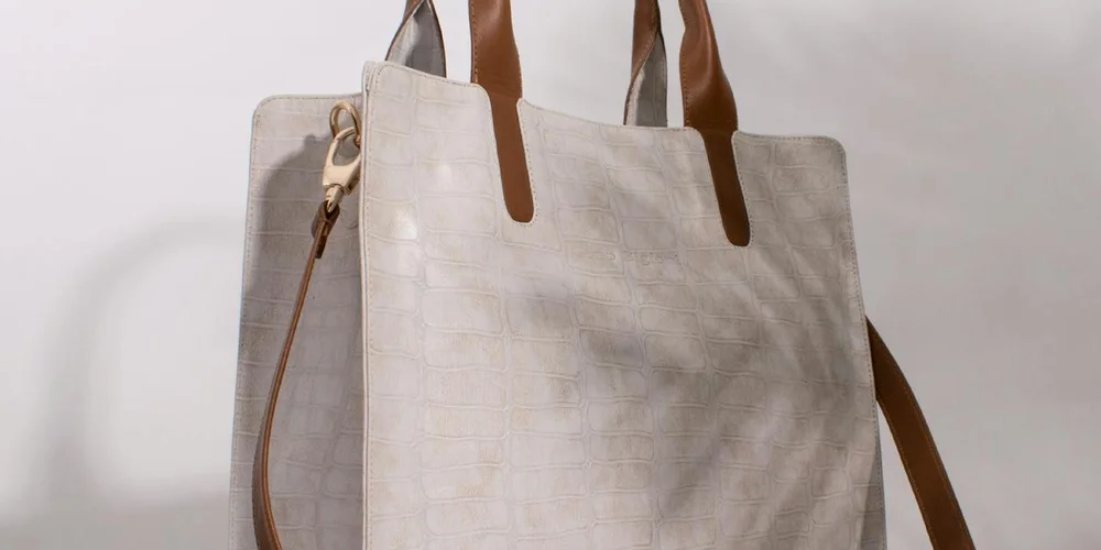 Beige tote bag with brown leather handles on a light background