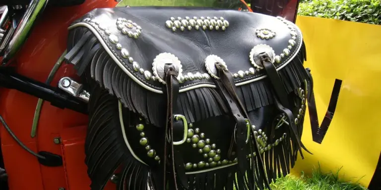A black leather bag with fringe and decorative metal studs sits outdoors.