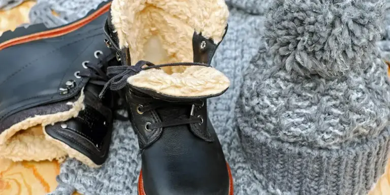 Close-up of black leather boots with cream shearling lining and metal eyelets, resting on a gray knitted surface.