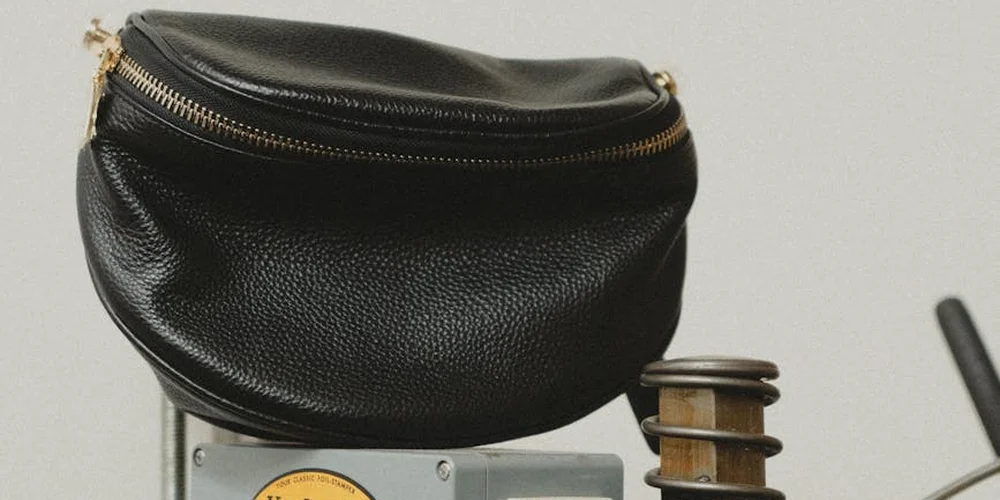 A black textured leather zippered pouch sitting on a small metal display stand against a light background.