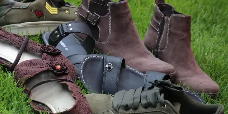 Several pairs of boots and shoes resting on green grass, featuring suede in brown and black tones and mixed materials.