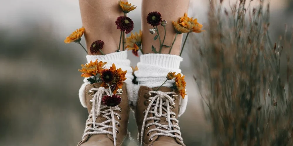 Brown suede boots with white laces, surrounded by dried flowers, outdoors in a field.
