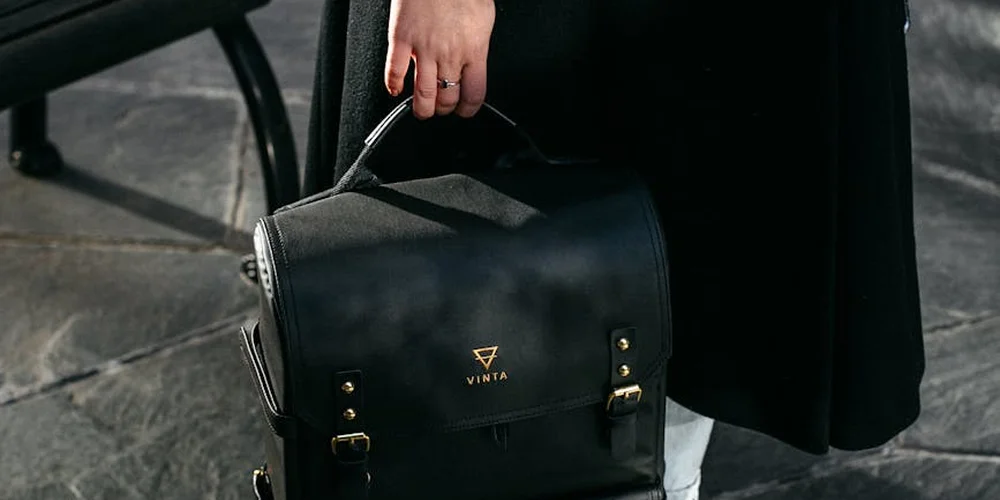 A black leather handbag with metal hardware being held outdoors, against a dark background.