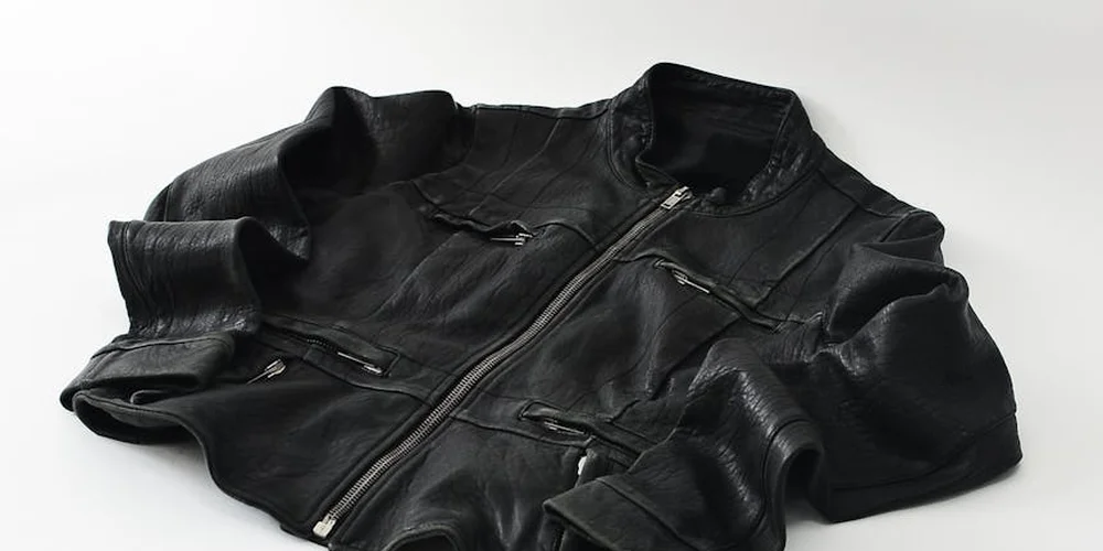 Black leather jacket laid flat on a white surface, showing creases and panel seams.