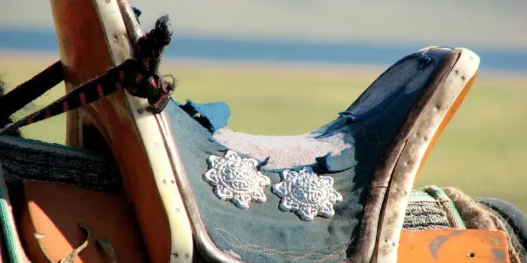 Close-up of a leather saddle with turquoise-blue saddle blanket and decorative silver conchos.