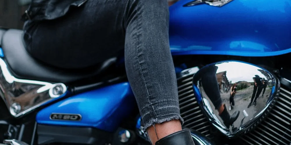 A rider in dark jeans sits on a blue motorcycle, illustrating a leather care context.