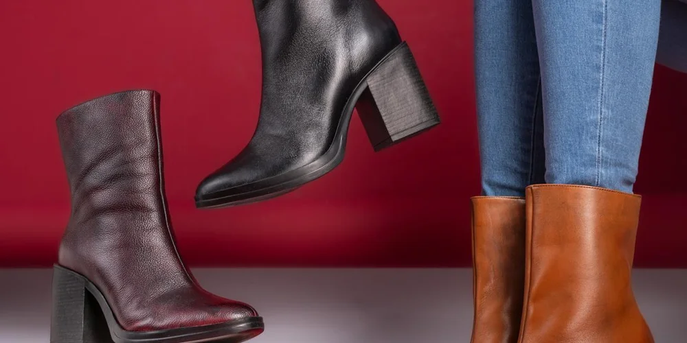 Three pairs of boots—burgundy ankle boot, black heeled boot, and tan leather boots—posed against a red backdrop.