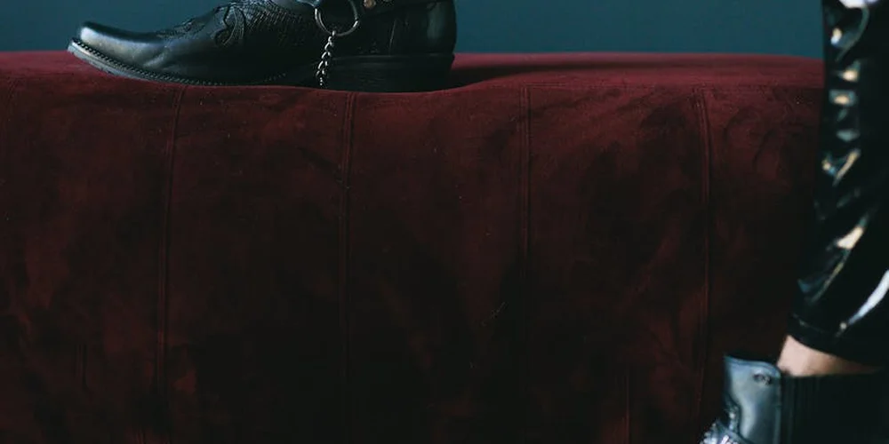 A black leather boot rests on a burgundy velvet surface, illustrating a scene for mink oil application on boots.