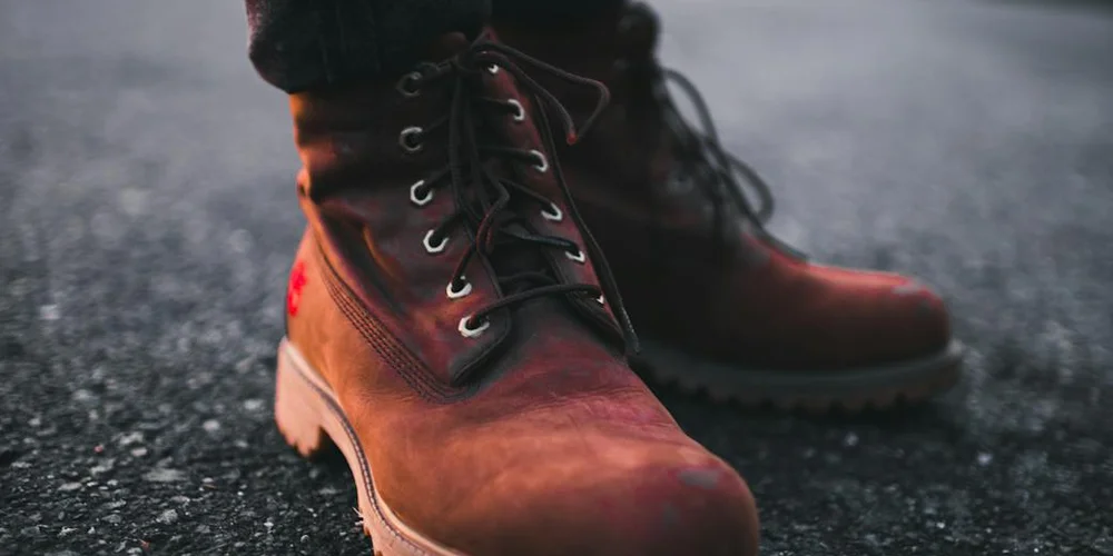 Close-up of brown leather lace-up boots resting on a wet pavement, highlighting the drying process after applying mink oil.
