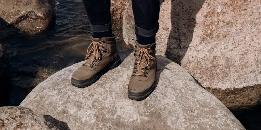 Brown leather hiking boots on large rocks beside a body of water.