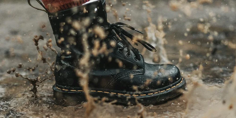 Black boot stepping through muddy ground with splashing mud droplets
