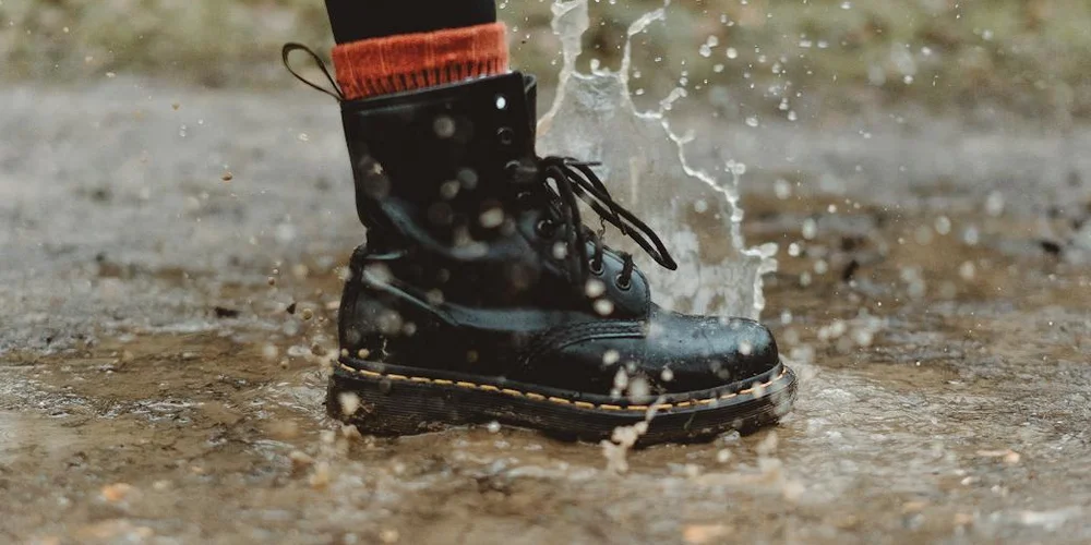A sturdy black leather boot splashing through a puddle on a cold, damp surface.
