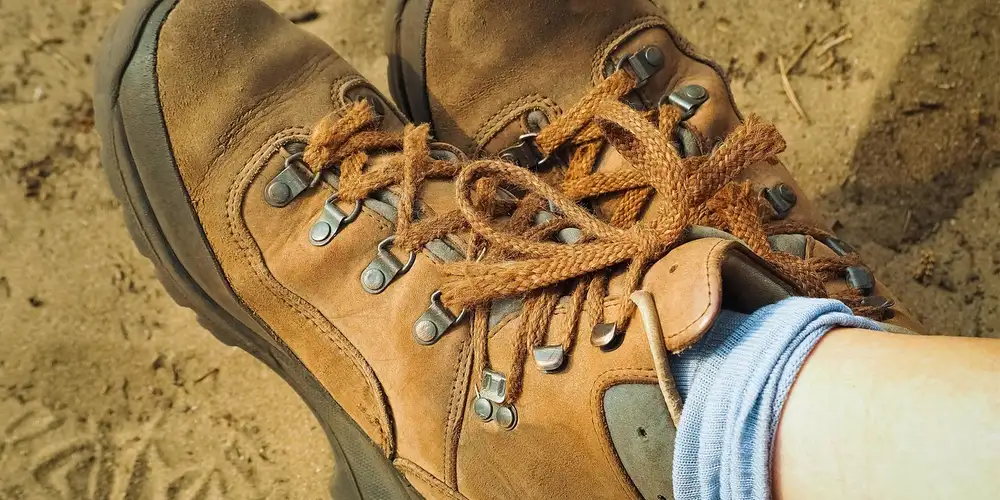 Brown leather hiking boots with tan laces resting on a dirt surface, showing metal eyelets and rugged sole
