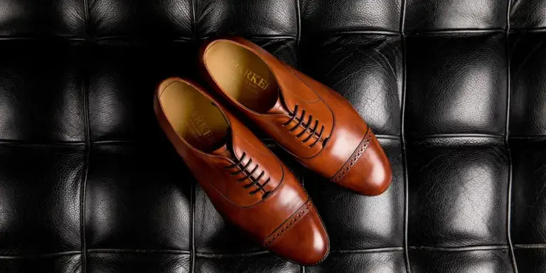 Pair of brown leather dress shoes with black stitching placed on a black quilted surface.