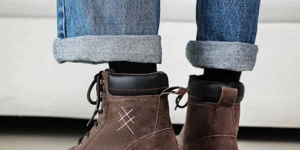 Brown suede lace-up boots with rolled cuffs resting on a light background.