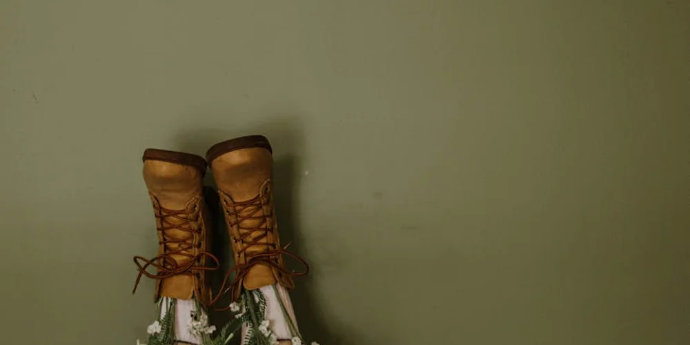Two brown lace-up boots on a muted green background, highlighting leather texture and construction.