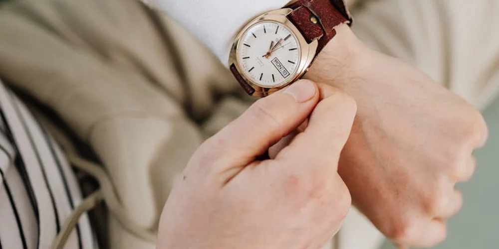 Close-up of a person adjusting a brown leather watch strap on their wrist