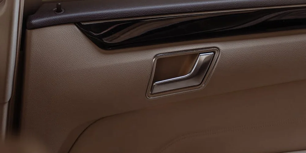 Close-up of a beige car door panel with textured faux leather material and a chrome door handle.