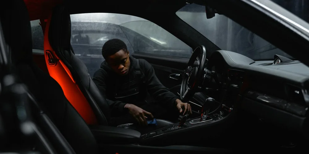 Person cleaning the leather interior of a car, focusing on the center console and seats