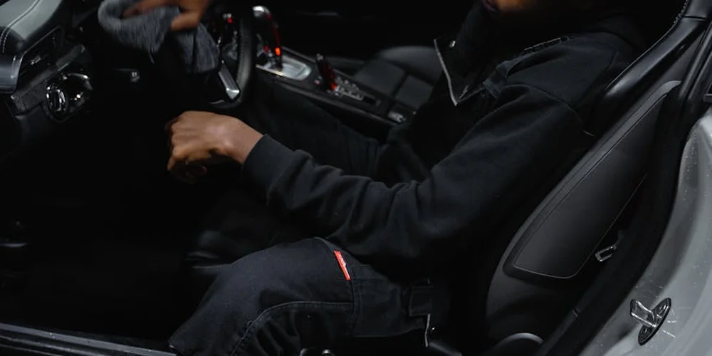 Person in dark clothing sitting in a car interior with leather seats and steering wheel visible.
