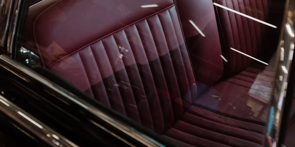 Close-up of burgundy car leather seats with visible wear and discoloration