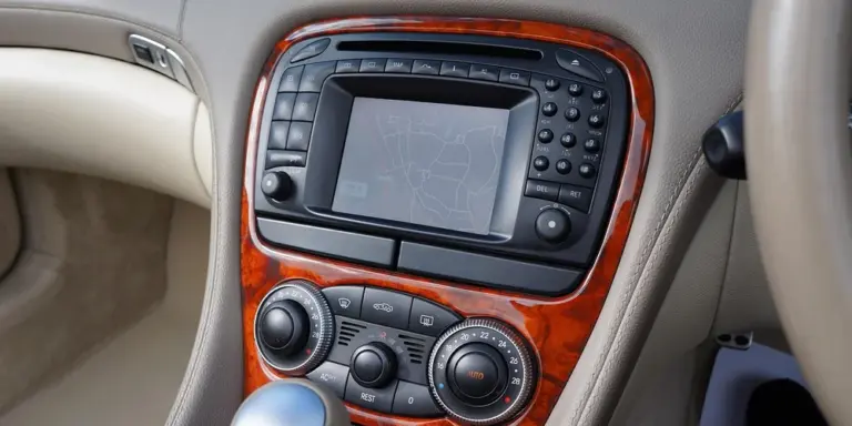 Close-up of a car interior center console with wood trim and climate controls, showing surrounding leather surfaces.