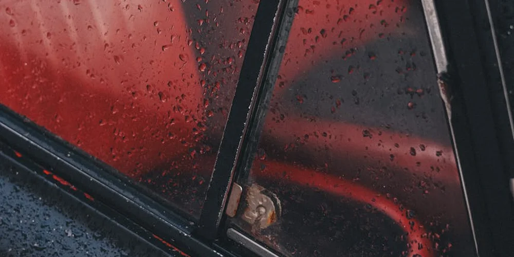 Close-up of a red leather car interior with water droplets on the window, highlighting wear on the surface.