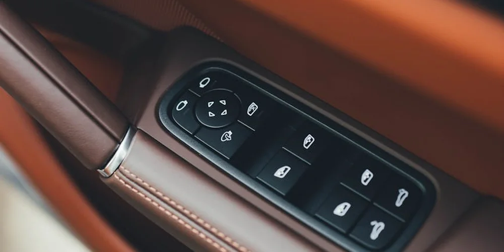 Close-up of brown leather car interior with window and seat control switches.