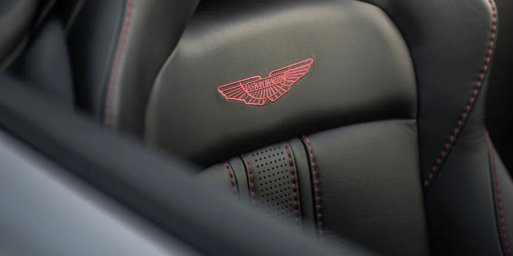 Close-up view of black leather car seat with red contrast stitching and a stitched emblem on the headrest