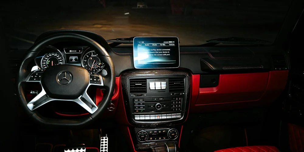 Night-time view of a Mercedes-Benz car interior featuring red-accent leather, a steering wheel, and a dashboard with a touchscreen.