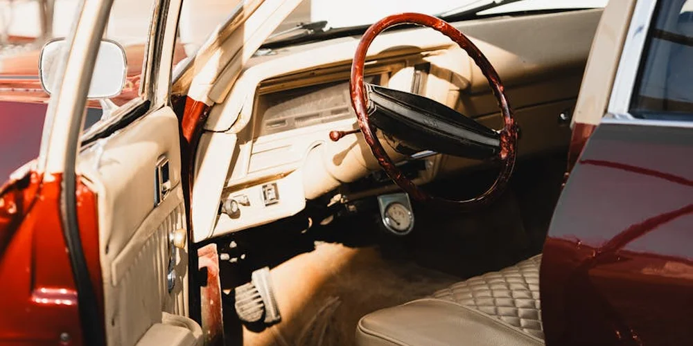 Interior of a vintage car with tan leather seats and a wooden steering wheel