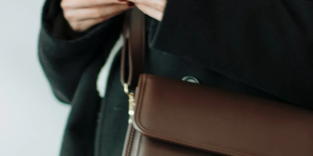 Close-up of a brown leather Coach handbag being held by a person wearing a black coat.