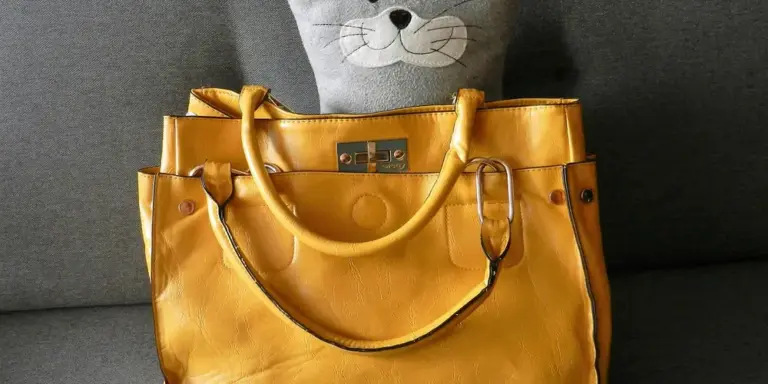 Mustard-yellow Coach leather handbag on a dark gray sofa with a plush gray cat toy in the background.