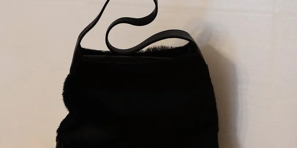 Black Coach leather handbag with a curved strap on a light background.