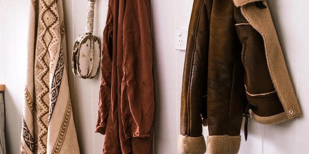 Several jackets and coats hanging on wall hooks in a hallway.