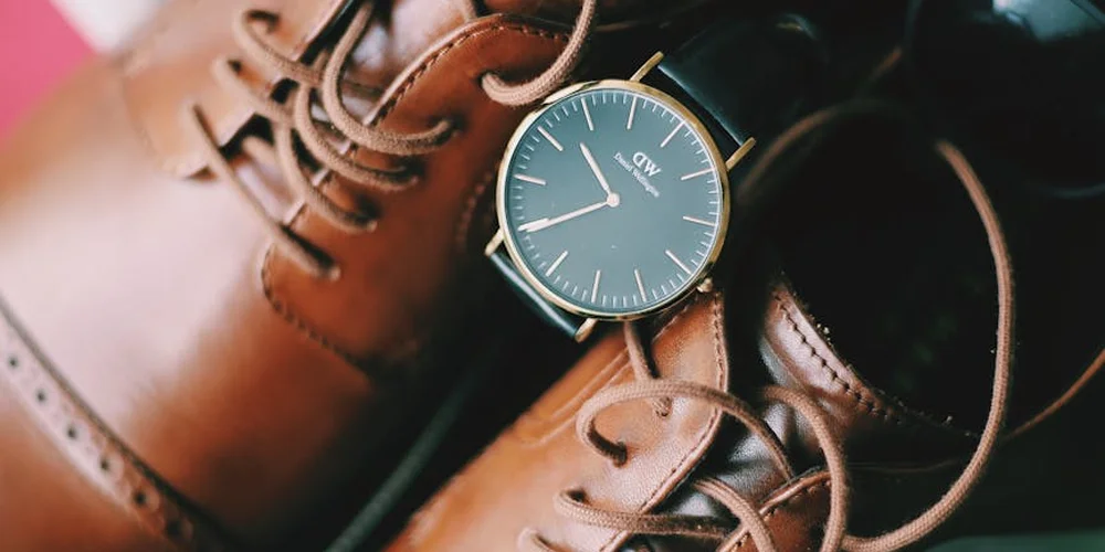Close-up of cognac leather shoes with a blue watch resting on top.