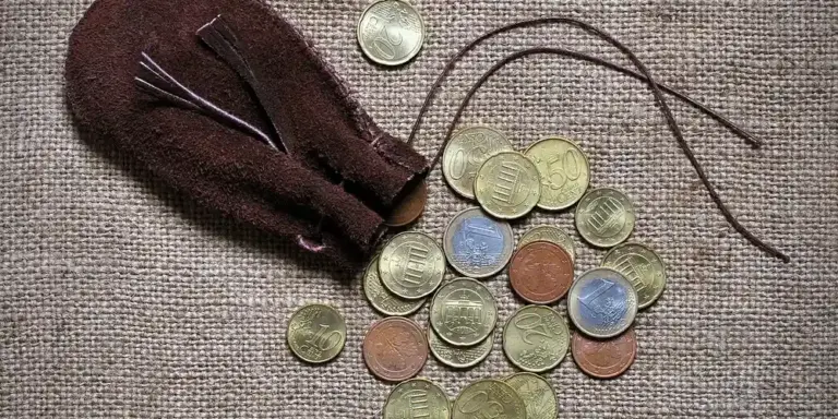 Close-up of a brown suede coin purse on a coarse burlap surface with scattered coins
