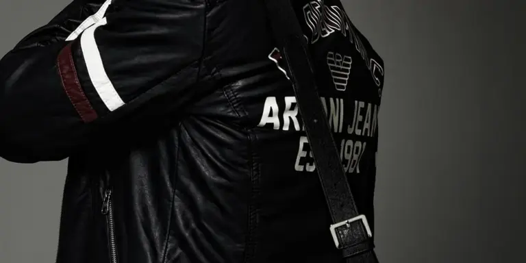 Close-up of a person wearing a black leather jacket with white piping and a strap across the chest.