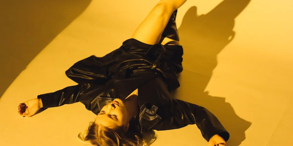 A person wearing a black leather jacket lying on a yellow studio floor