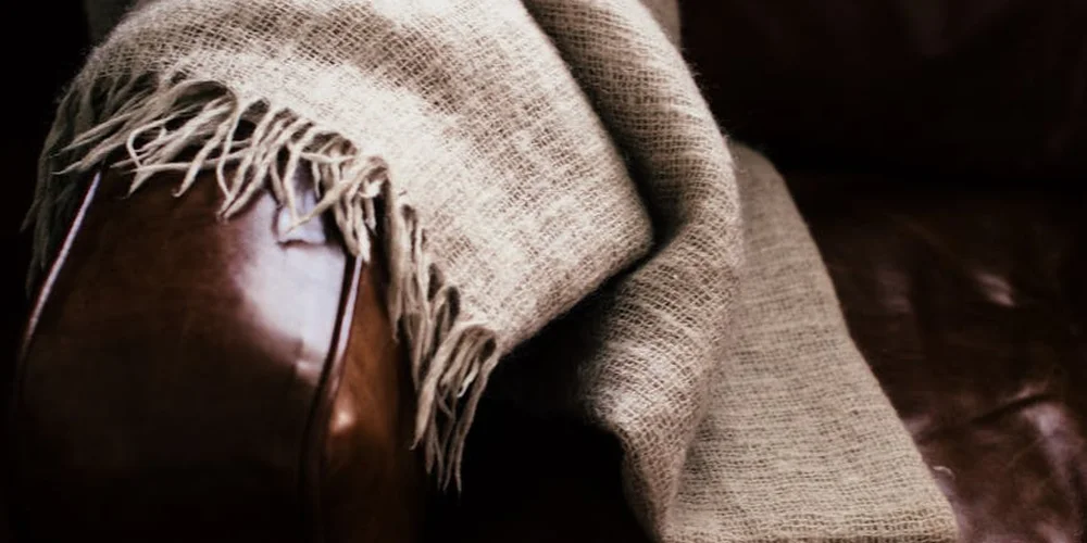 Close-up of brown cowhide leather upholstery with a beige woven throw blanket draped over it.