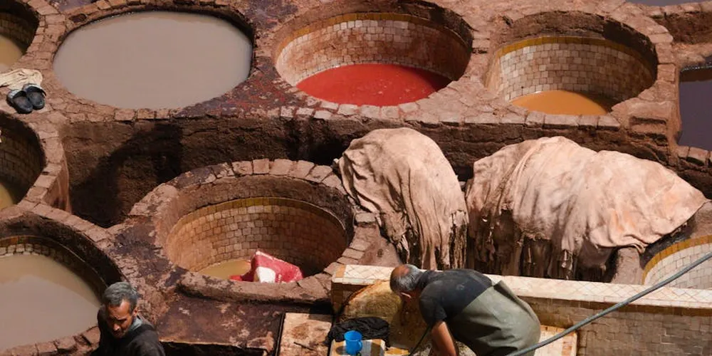 Interior of a leather tannery showing large circular vats with colored tanning liquids and hides draped over equipment as workers attend to the process.