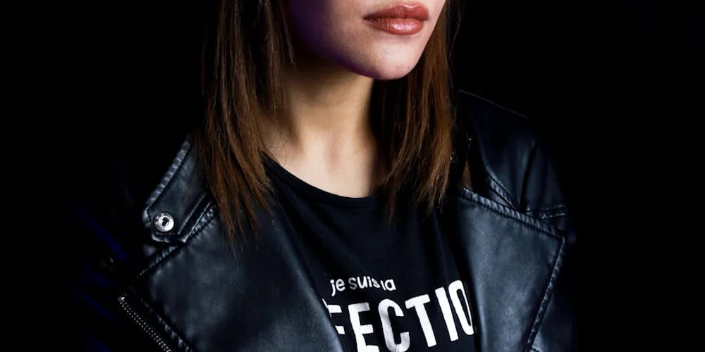 Close-up of a person wearing a black faux leather jacket over a black T-shirt with white text