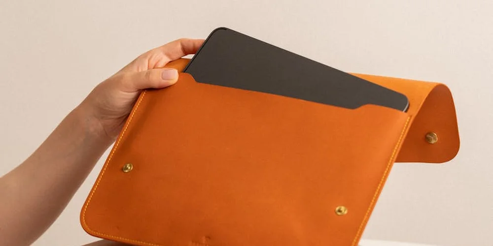 Close-up of a hand holding an orange faux leather organizer with a gray card inside.