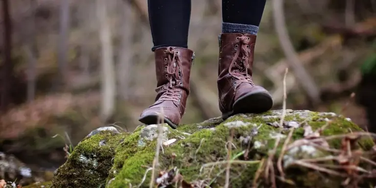 Brown leather boots standing on a moss-covered rock in a forest trail.