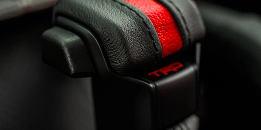 Close-up of a black leather interior with a red accent and a dark plastic component, illustrating leather surfaces where gum may adhere.
