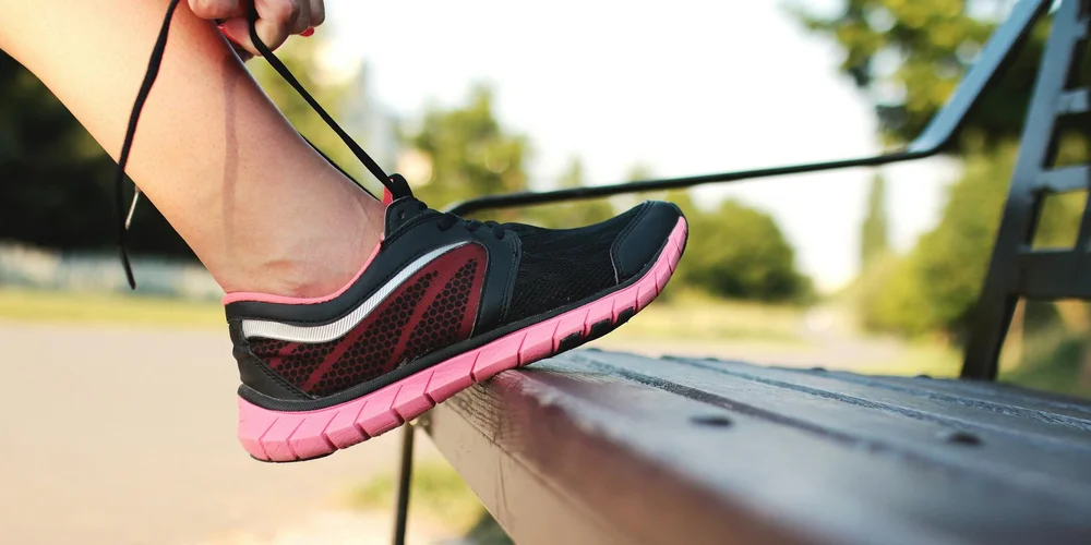 Outdoors, a person tying a black and pink suede Jordan sneaker with a pink sole, illustrating care-focused imagery