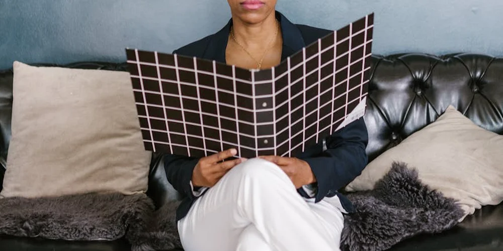 A person sits on a black tufted leather sofa, holding a large grid-pattern panel in front of their torso.